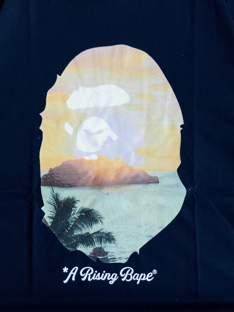 BAPE A Rising Bape Sunset Graphic Tee Black (Category: Tshirts & Polo Shirts ) located in Batangas. Submitted by rafstaywitstaff_11 (Listing ID 1468585107, Image 2). Description: - Brand: A Bathing Ape (BAPE) - Color: Black - Style: Short sleeve t-shirt - Design: Large sunset beach graphic inside signature ape head with 'A Rising Bape' text - Details: Small ape head logo tag on left sleeve hem - Condition: Brand new with hang tag attached.