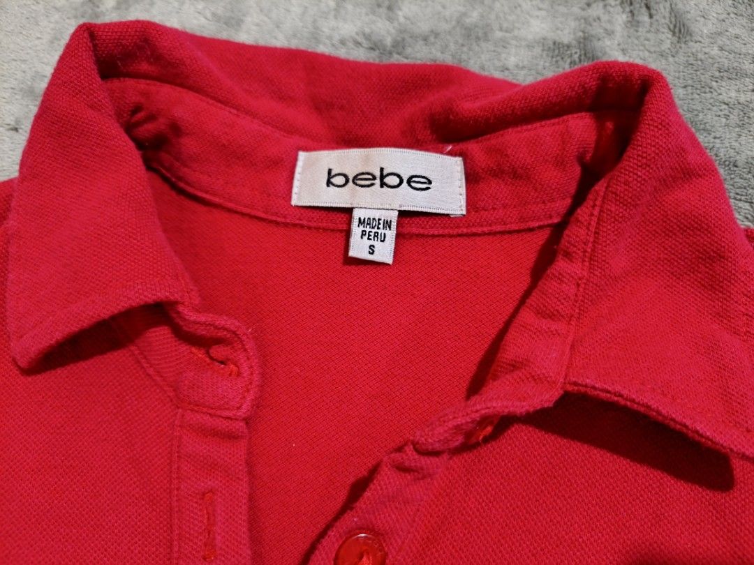Bebe (Category: Shirts) located in Bacolod City. Submitted by loothingsph (Listing ID 1468678906, Image 3). Description: Bright red polo shirt from bebe. Size small. Made in Peru. Cotton and spandex blend, so it has some stretch. Sparkly rhinestone bebe logo on the chest. Classic collar with a three-button placket. Extra button attached to the inner care tag. Short sleeves. Ribbed fabric texture..