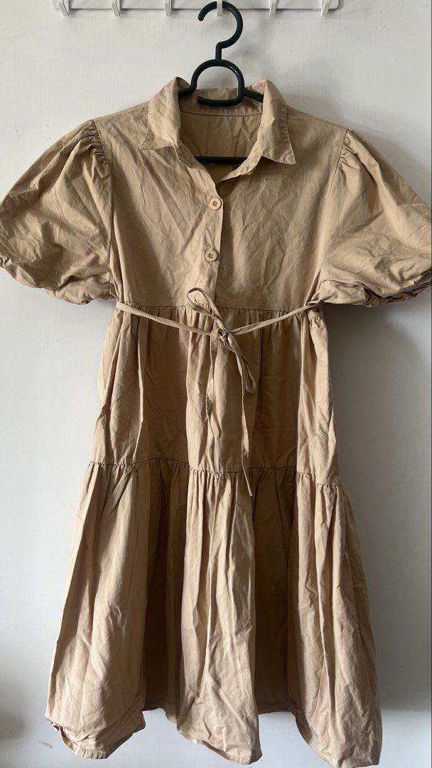 Beige Collared Puff Sleeve Tiered Dress (Category: Dresses) located in Taguig. Submitted by xkmanzano078817 (Listing ID 1468511139, Image 2). Description: Beige dress with a sharp shirt collar and short puff sleeves. Button-down front placket with two buttons visible. Includes a matching fabric tie belt at the waist. Skirt falls in a tiered, flared silhouette. Lightweight cotton-blend fabric. Length hits above the knee..