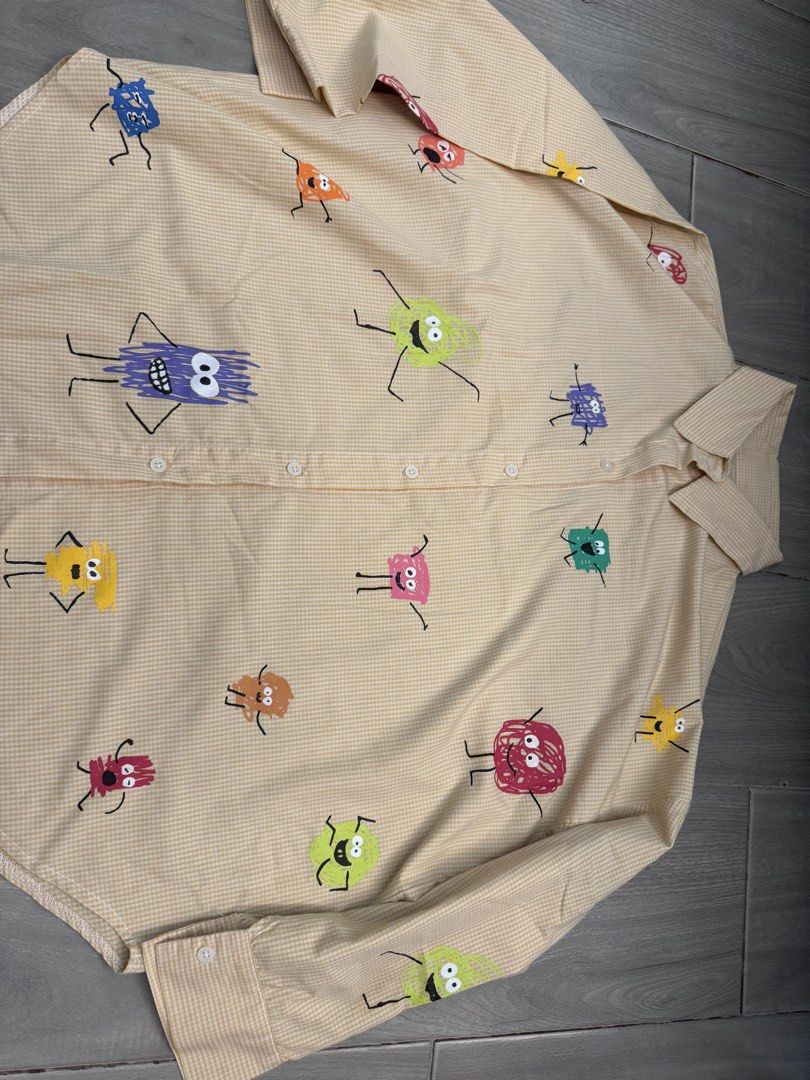Beige Gingham Button-Up Shirt With Cute Doodle Monsters (Category: Shirts) located in Taguig. Submitted by sqaumejada (Listing ID 1468527276, Image 1). Description: - Style: Long-sleeve button-up shirt with classic collar and buttoned cuffs - Pattern: Beige and white gingham with colorful doodle monster graphics, googly eyes, and stick legs - Fit: Standard button-front closure - Vibe: Fun, quirky statement piece - Condition: Clean and ready to we