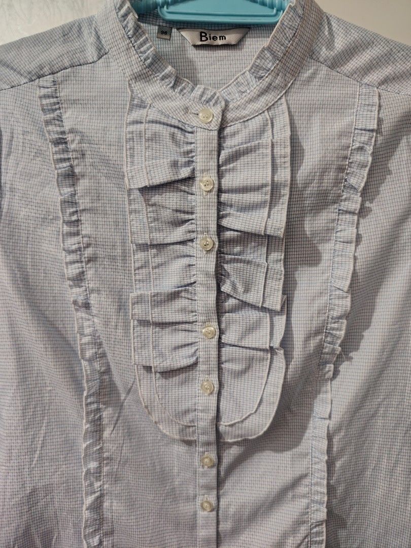 Biem Light Blue Checkered Ruffled Button-Down Blouse Size 36 (Category: Blouses) located in Valenzuela. Submitted by zealstar.48eb73 (Listing ID 1468668957, Image 2). Description: - Brand: Biem - Color: Light blue checkered - Size: 36 - Style: Long-sleeve fitted blouse with vertical panels - Details: Mandarin collar with front pleated ruffle accents and small white buttons - Condition: Excellent, clean fabric with no stains or loose threads - Mod