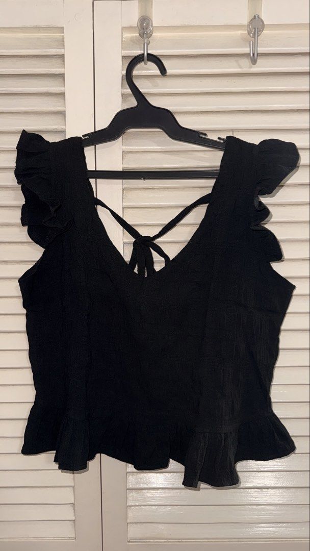 Black Ruffle Strap Crop Top with Tie Back (Category: Sleeveless) located in Manila. Submitted by oliviablanche (Listing ID 1468607186, Image 1). Description: - Color: Black - Style: Crop top with V-neckline (front & back) - Details: Wide ruffle straps, ruffle hem, and secure back-tie cross straps - Fabric: Textured with slight stretch for comfort - Versatility: Great for daily wear; easy to match with jeans or high-waisted skirts - Condition: Lik