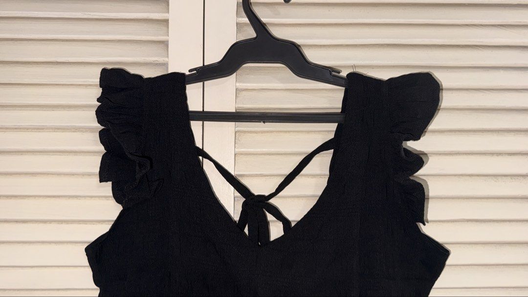 Black Ruffle Strap Crop Top with Tie Back (Category: Sleeveless) located in Manila. Submitted by oliviablanche (Listing ID 1468607186, Image 3). Description: - Color: Black - Style: Crop top with V-neckline (front & back) - Details: Wide ruffle straps, ruffle hem, and secure back-tie cross straps - Fabric: Textured with slight stretch for comfort - Versatility: Great for daily wear; easy to match with jeans or high-waisted skirts - Condition: Lik