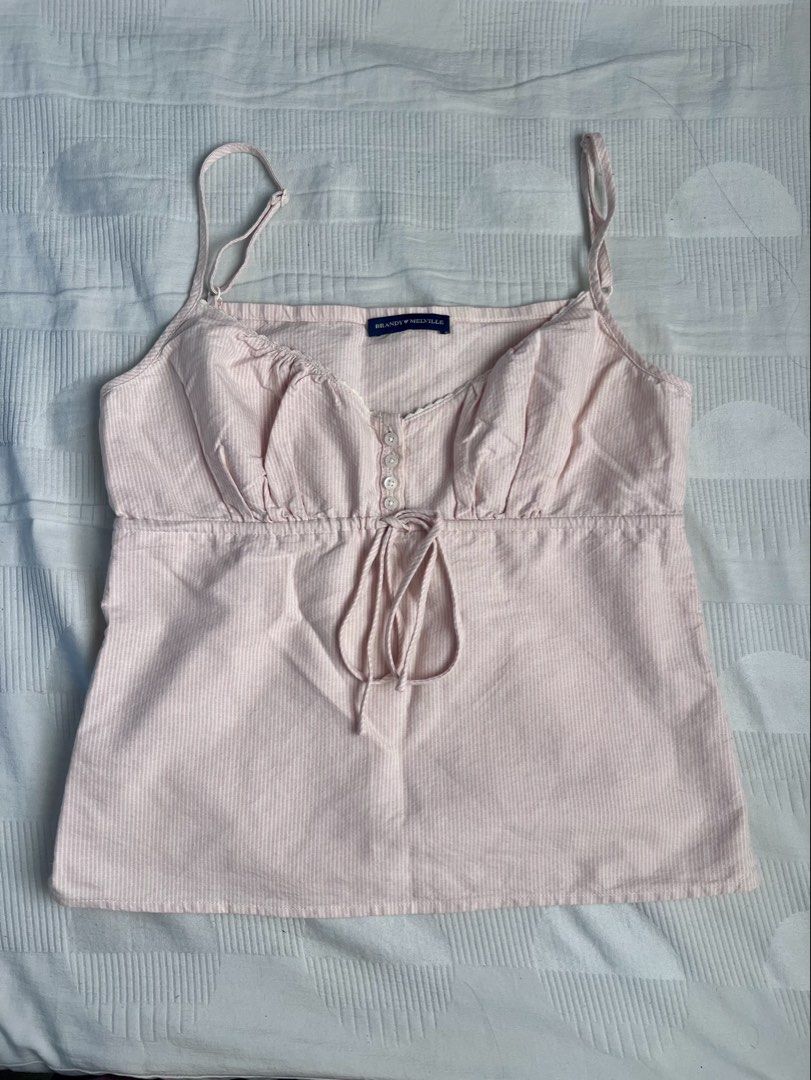 Brandy Melville Tiffany Top (Category: Sleeveless) located in Manila. Submitted by sh4rice (Listing ID 1468547060, Image 1). Description: - Brand: Brandy Melville (Tiffany Top) - Color: Light pink with subtle white stripes - Features: Adjustable spaghetti straps, decorative front buttons, and a front ribbon tie .