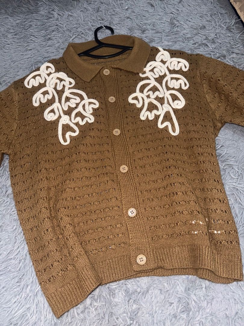 Brown Knitted Shirt (Category: Coats, Jackets and Outerwear) located in Quezon City. Submitted by ashhaul (Listing ID 1468563186, Image 2). Description: - Style: Short-sleeve knit cardigan with button closure - Details: White embroidered floral pattern on the chest, open-work details on the bottom hem - Size: L (tag attached) - Color: Brown (cozy neutral) - Condition: Excellent, easy to match with various outfits - From Shein.
