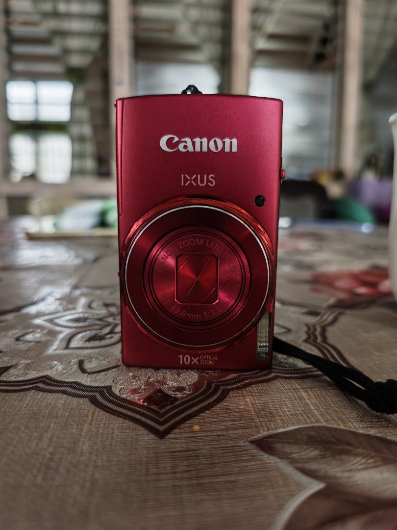 Canon IXUS 155 Digital Camera (Category: Cameras) located in Batangas. Submitted by cvllanda (Listing ID 1468520695, Image 2). Description: - Model: Red Canon IXUS compact digital camera - Zoom: 10x optical zoom for clear distance shots - Condition: Fully functional, 95% smooth, no cover on usb port - Portability: Compact body that easily fits in your pocket - Included Accessories: Battery, charger, attached wrist strap, and a black Case Logic zi