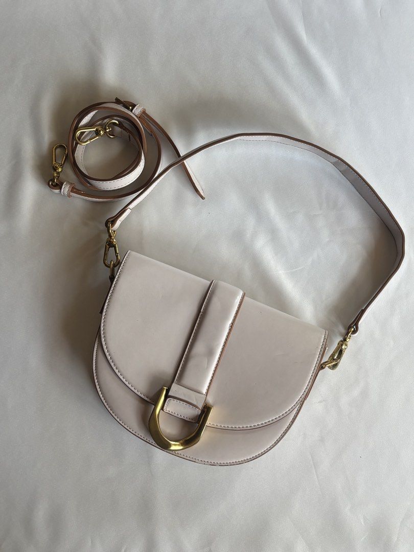 Charles & Keith Saddle Bag White (Category: Shoulder Bags) located in Iloilo. Submitted by iconicangie (Listing ID 1468555315, Image 3). Description: - Style: White saddle bag with sleek brown contrast edging - Hardware: Elegant gold-tone accents and a distinctive U-shaped metal ring front closure - Material: Premium faux leather with a clean interior lining - Versatility: Includes an adjustable shoulder strap and a separate shorter handle option