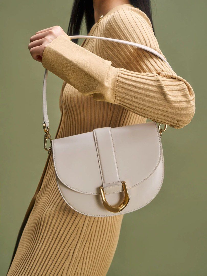 Charles & Keith Saddle Bag White (Category: Shoulder Bags) located in Iloilo. Submitted by iconicangie (Listing ID 1468555315, Image 2). Description: - Style: White saddle bag with sleek brown contrast edging - Hardware: Elegant gold-tone accents and a distinctive U-shaped metal ring front closure - Material: Premium faux leather with a clean interior lining - Versatility: Includes an adjustable shoulder strap and a separate shorter handle option
