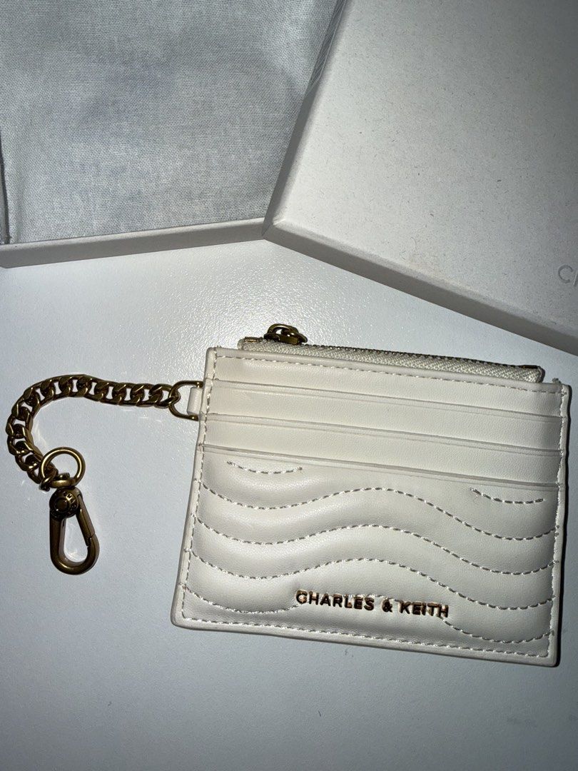 Charles & Keith White Card Holder with Chain (Category: Wallets & Card holders) located in Manila. Submitted by chi.declutter (Listing ID 1468517148, Image 2). Description: Bought at 1400 now selling for 1100 - Brand: Charles & Keith - Color: White with elegant gold hardware - Design: Quilted wave pattern at the bottom - Compartments: Zipper top compartment and multiple front card slots - Extras: Attached metal chain with lobster clasp clip - Inc
