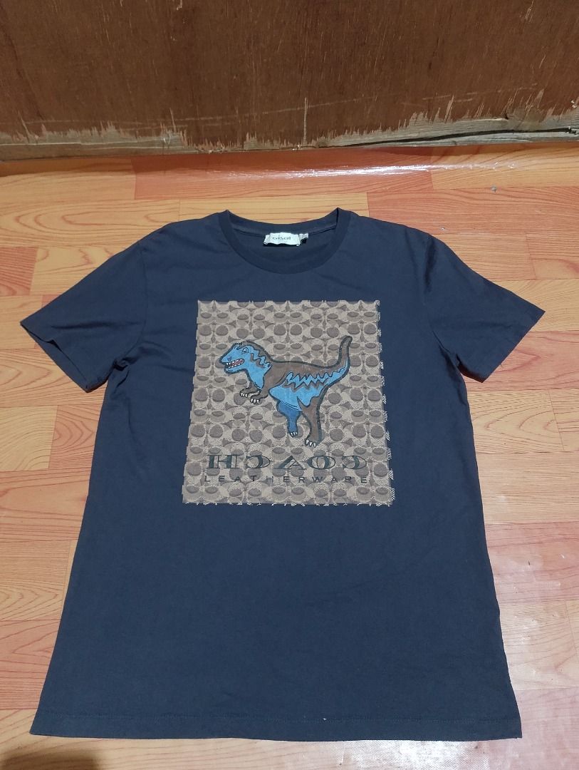 Coach 1941 Dinosaur Graphic Tee Navy Size M (Category: Tshirts & Polo Shirts ) located in Cavite. Submitted by marvzclothing (Listing ID 1468613803, Image 1). Description: - Brand: Coach 1941 - Item: Graphic T-Shirt with Rexy Dinosaur and Monogram Pattern - Color: Dark Navy Blue - Size: Medium - Origin: Made in Peru - Details: Leather Coach story patch near hem, clean fabric, tags fully intact - Style: Casual streetwear with classic designer bran