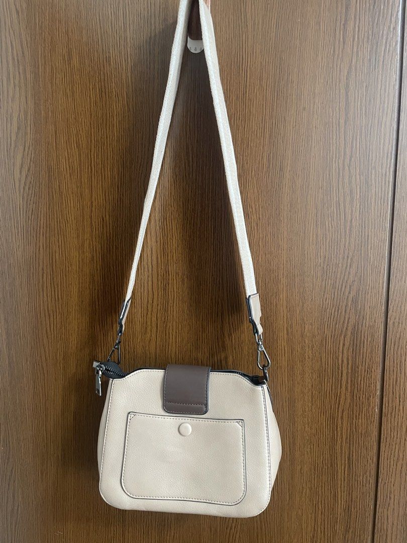 Cream and Brown Crossbody Bag (Category: Cross-body Bags) located in Manila. Submitted by misyeli (Listing ID 1468552866, Image 3). Description: - Color: Cream and brown - Closure: Structured front flap with geometric buckle accent - Branding: Gold-tone foil print near the front base - Strap: Adjustable matching shoulder strap - Pocket: Convenient snap-button pocket on the back - Condition: Brand new / Excellent (ready to ship!).