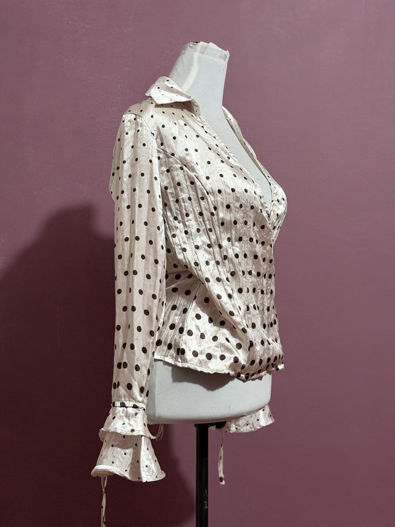 Cream Polka Dot Top Blouse with Ruffle Cuffs (Category: Blouses) located in Manila. Submitted by thatgirl0001 (Listing ID 1468592570, Image 2). Description: - Color & Pattern: Cream with all-over black polka dots - Design: Wrap front style with V-neckline and pointed collar - Sleeves: Long sleeves with double ruffle cuffs and string ties - Fabric: Lightweight silky material with a subtle vertical texture - Style: Retro vibe, easily pairs with ski