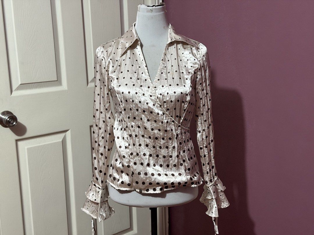 Cream Polka Dot Top Blouse with Ruffle Cuffs (Category: Blouses) located in Manila. Submitted by thatgirl0001 (Listing ID 1468592570, Image 1). Description: - Color & Pattern: Cream with all-over black polka dots - Design: Wrap front style with V-neckline and pointed collar - Sleeves: Long sleeves with double ruffle cuffs and string ties - Fabric: Lightweight silky material with a subtle vertical texture - Style: Retro vibe, easily pairs with ski