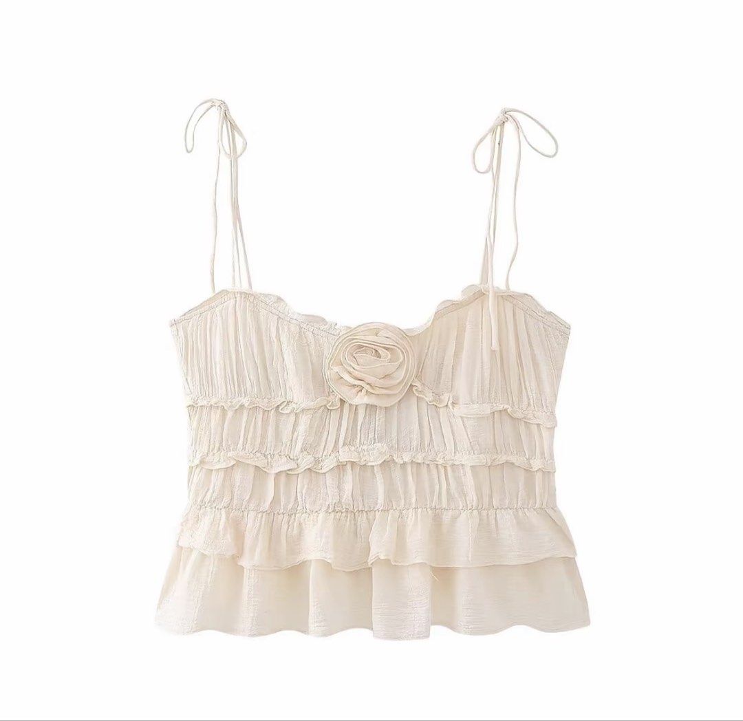 Cream Ruffled Camisole with Rosette Detail (Category: Sleeveless) located in Marikina City. Submitted by RestyledStore (Listing ID 1468566328, Image 2). Description: - Color: Cream - Design: Layered ruffles with a charming 3D chest rosette and flared hem - Straps: Adjustable tie shoulder straps for a custom fit - Fabric: Lightweight and textured - Styling: Pairs effortlessly with denim skirts or high-waisted jeans - Size : Small.