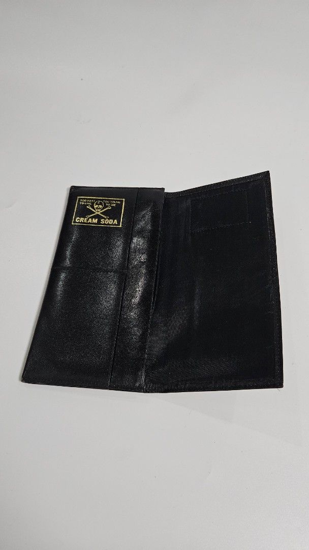 Cream Soda Black Leather Long Wallet (Category: Wallets & Card Holders) located in Alfonso. Submitted by jbcamet (Listing ID 1468652110, Image 3). Description: - Brand: Cream Soda - Material: Smooth black leather - Design: Red exterior label with skull & crossbones and "Too Fast To Live Too Young To Die" text - Interior: Gold skull print with multiple card slots and cash compartments - Condition: Clean stitching and well-maintained - Perfect for 