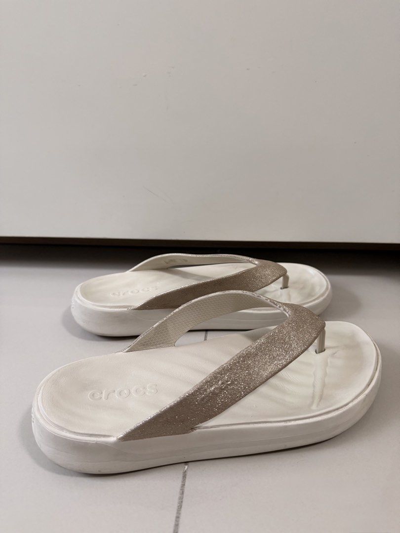 Crocs Glitter Thong Sandals Size W7 (Category: Slippers and slides) located in Quezon City. Submitted by eya_preloved (Listing ID 1468580380, Image 2). Description: - Brand: Crocs - Style: Platform flip-flops - Color: White with champagne gold sparkly straps - Size: Women's 7 - Features: Super lightweight foam footbed with textured grip - Condition: Clean footbeds, minor wear on bottom treads from brief outdoor use - Perfect for: Summer outings a