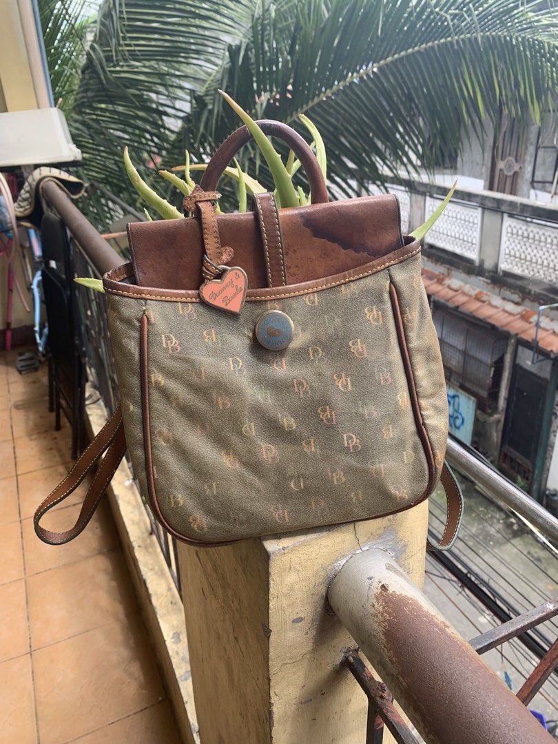 Dooney & Bourke Monogram Mini Backpack (Category: Backpacks) located in Pasig City. Submitted by cool.itshara (Listing ID 1468551212, Image 1). Description: - Brand: Dooney & Bourke - Style: Mini backpack - Color: Olive green monogram print with brown leather accents - Features: Flap top, top handle, adjustable shoulder straps, and cute heart-shaped front charm - Hardware: Durable metal accents - Condition: Excellent / Well-maintained - Perfect f