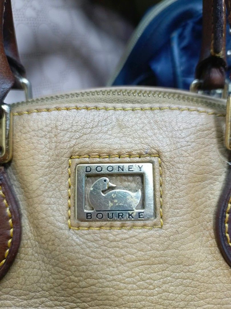 Dooney & Bourke Tan Leather Shoulder Bag (Category: Luxury Bags & Wallets) located in Manila. Submitted by dei03_diz (Listing ID 1468543956, Image 2). Description: - Brand: Dooney & Bourke - Material: Tan pebbled leather with brown leather trim - Hardware: Iconic metal duck logo plaque on front, Riri zipper closure - Interior: Pink checkered fabric lining with a zipper pocket and brand tag - Condition: Shows natural wear on the leather and slight