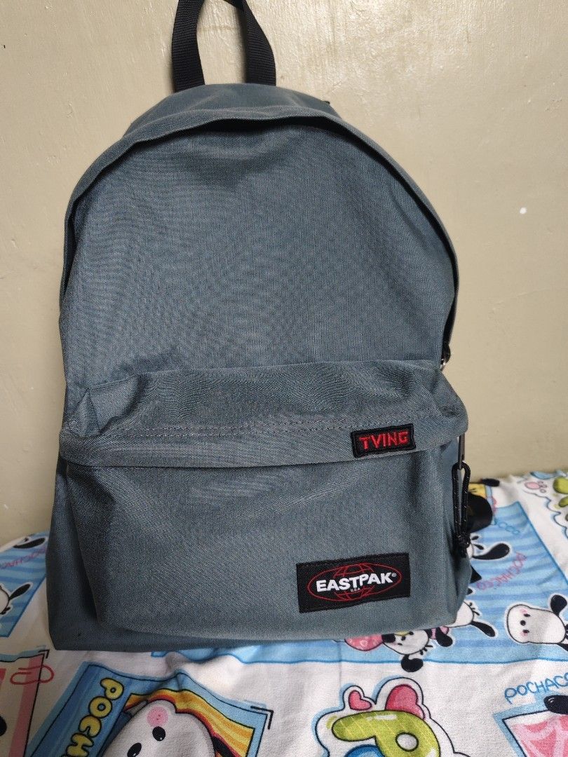 Eastpak Grey Backpack with TVING Patch (Category: Backpacks) located in General Mariano Alvarez. Submitted by findsandmoreph (Listing ID 1468647963, Image 1). Description: Grey Eastpak backpack with adjustable black shoulder straps. Features a front zipped pocket adorned with a red TVING patch. Main compartment zips open smoothly with interior fabric lining and tag labels inside. Clean textured canvas material throughout. Durable top handle inclu