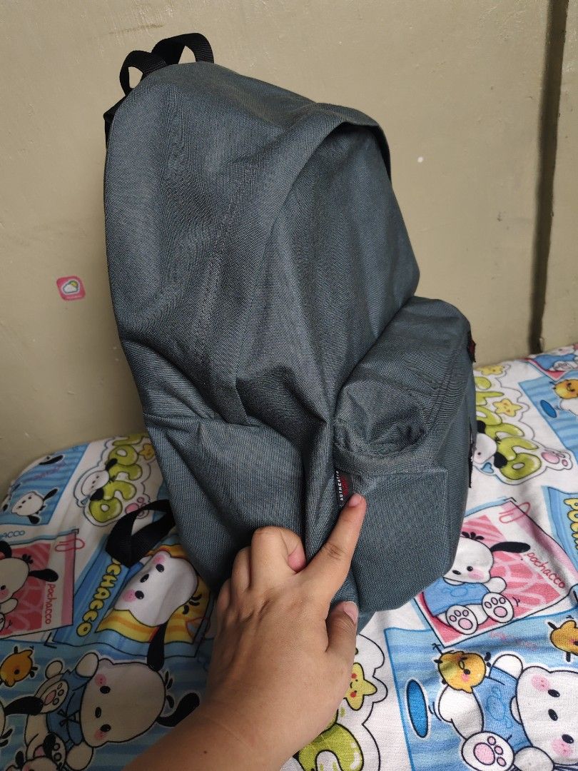 Eastpak Grey Backpack with TVING Patch (Category: Backpacks) located in General Mariano Alvarez. Submitted by findsandmoreph (Listing ID 1468647963, Image 3). Description: Grey Eastpak backpack with adjustable black shoulder straps. Features a front zipped pocket adorned with a red TVING patch. Main compartment zips open smoothly with interior fabric lining and tag labels inside. Clean textured canvas material throughout. Durable top handle inclu