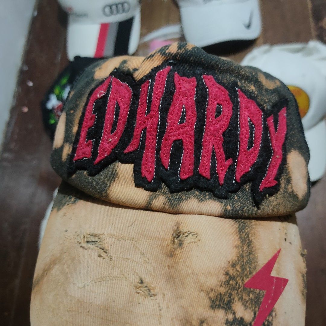 Ed Hardy Acid Wash Distressed Trucker Cap (Category: Caps & Hats) located in Taguig. Submitted by actualizeboutique (Listing ID 1468524754, Image 2). Description: - Brand: Ed Hardy - Style: Trucker cap with distressed acid wash finish and heavy wear on the brim - Details: Bright red embroidered front logo and small pink lightning bolt graphic on the right side - Back: Black mesh panel with adjustable snapback closure - Branding: Embroidered scrip