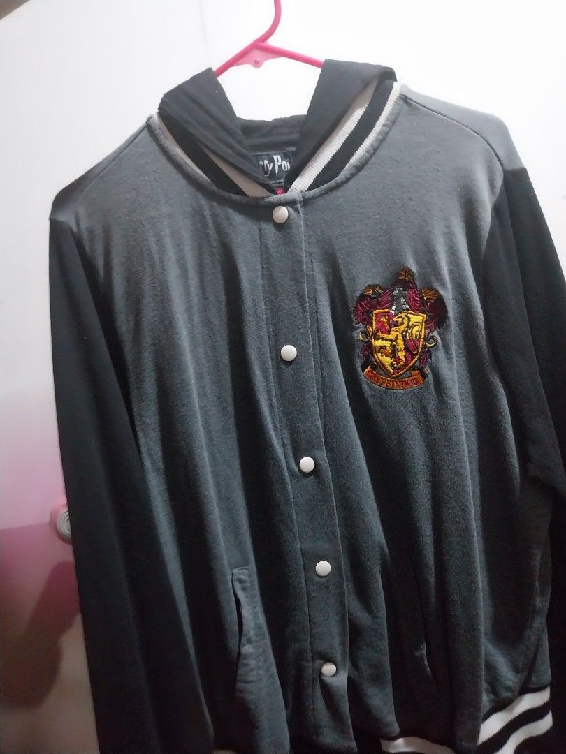 Harry Potter Gryffindor Varsity Jacket official merch (Category: Coats, Jackets and Outerwear) located in Manila. Submitted by j.dlh (Listing ID 1468662836, Image 1). Description: - Official Harry Potter Gryffindor varsity jacket - Color: Grey and black with an attached black hood - Embroidered Gryffindor crest on the chest - Vertical 'POTTER' lettering on the back in yellow and maroon - Snap button front closure - Striped ribbed collar, cuffs, a