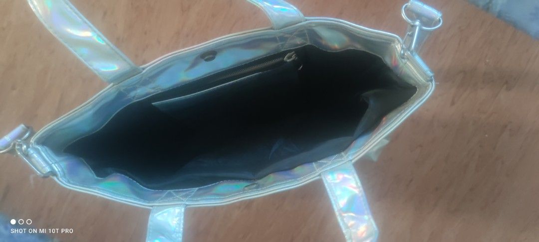 Holographic Metallic Tote Bag with Shoulder Strap (Category: Tote Bags) located in Cavite. Submitted by Combiishop (Listing ID 1468557703, Image 3). Description: - Eye-catching shiny holographic metallic finish that shifts color in the light - Versatile design with short carry handles and a detachable long shoulder strap - Secure top snap button closure with sleek silver hardware - Spacious main compartment lined in black fabric - Convenient zipp