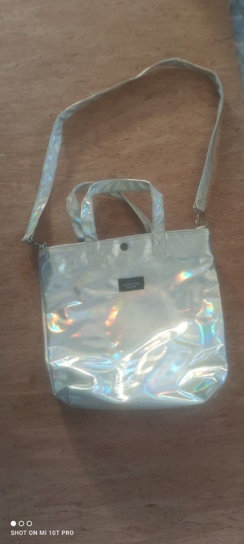 Holographic Metallic Tote Bag with Shoulder Strap (Category: Tote Bags) located in Cavite. Submitted by Combiishop (Listing ID 1468557703, Image 1). Description: - Eye-catching shiny holographic metallic finish that shifts color in the light - Versatile design with short carry handles and a detachable long shoulder strap - Secure top snap button closure with sleek silver hardware - Spacious main compartment lined in black fabric - Convenient zipp