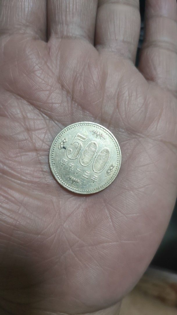 Japanese 500 Yen Coin (Category: Currency) located in Caloocan City. Submitted by joshuadyogi0122 (Listing ID 1468507084, Image 1). Description: Japanese 500 yen coin resting in an open palm. Face shows 500 numerals and Japanese characters. Reverse displays a paulownia plant design with leaves and flowers. Standard currency size, metallic finish with minor signs of handling. Great piece for coin collectors or anyone needing Japanese currency..
