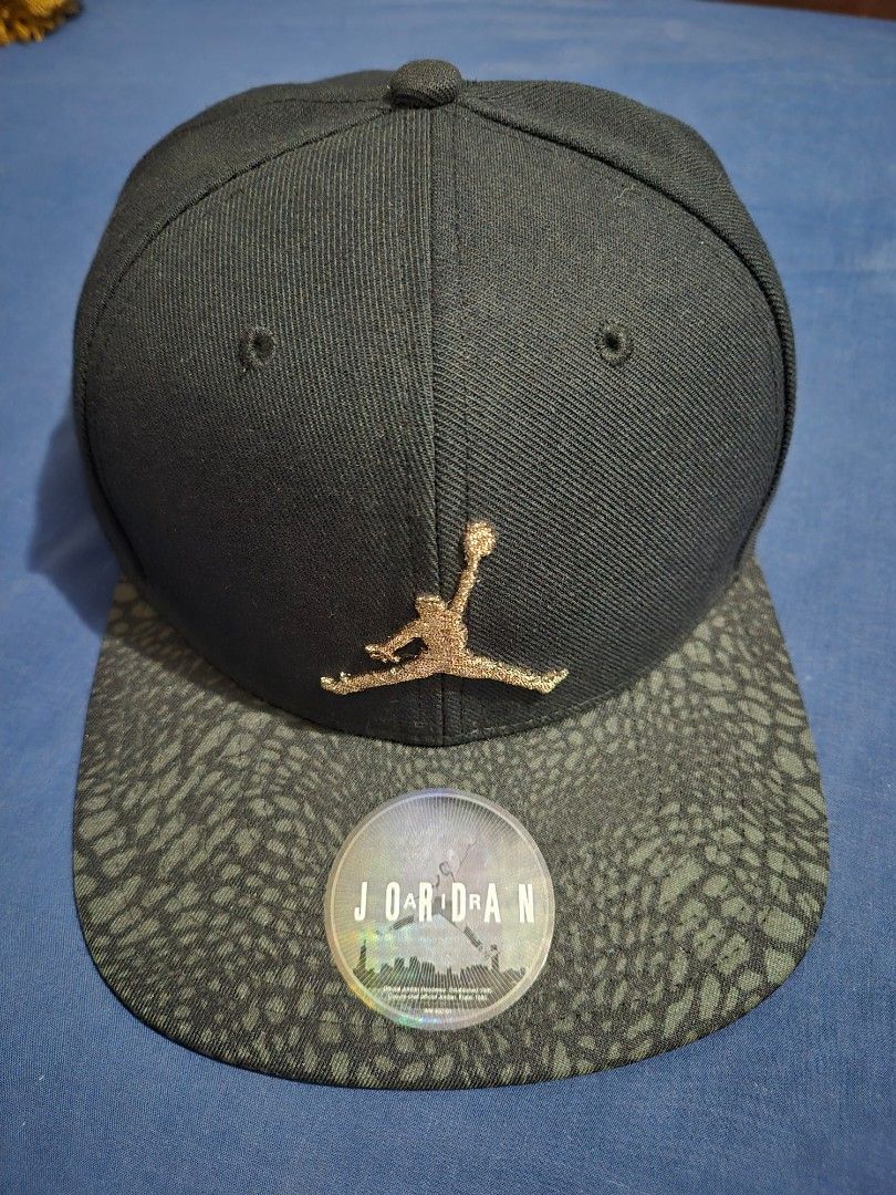 Jordan Jumpman Strapback Cap Black Bronze Elephant Bill (Category: Caps & Hats) located in Pasig City. Submitted by lordcajayon (Listing ID 1468679629, Image 3). Description: - Brand: Jordan - Color: Black with dark grey elephant print brim - Logo: Textured gold Jumpman logo on the front - Authenticity: Includes official hologram sticker on the brim - Fit: Adjustable strap at the back with a metal clasp and small Jumpman tag - Details: Inside tap