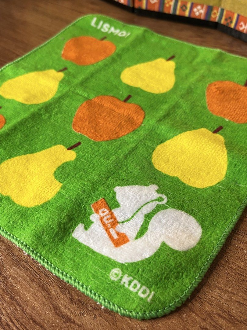 KDDI LISMO Green Fruit Pattern Towel (Category: Towels, Napkins & Holders) located in Gapan. Submitted by lunashop14 (Listing ID 1468693191, Image 2). Description: Green hand towel with colorful fruit pattern featuring apples, pears, and a white squirrel graphic holding an orange au. logo. Brand text LISMO! printed at top left corner and KDDI logo at bottom right. Reverse side is plain white terry cloth. Soft fabric texture. Fun retro promotional