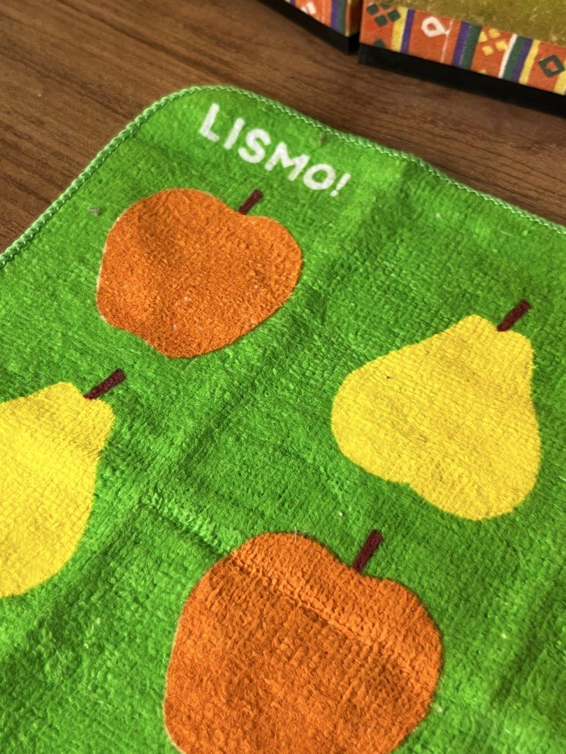 KDDI LISMO Green Fruit Pattern Towel (Category: Towels, Napkins & Holders) located in Gapan. Submitted by lunashop14 (Listing ID 1468693191, Image 3). Description: Green hand towel with colorful fruit pattern featuring apples, pears, and a white squirrel graphic holding an orange au. logo. Brand text LISMO! printed at top left corner and KDDI logo at bottom right. Reverse side is plain white terry cloth. Soft fabric texture. Fun retro promotional