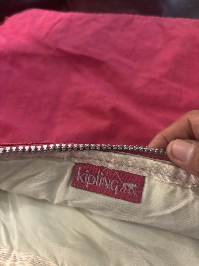 Kipling Pink Pouch (Category: Purses & Pouches) located in Manila. Submitted by jeromskito66462 (Listing ID 1468666896, Image 2). Description: - Brand: Kipling - Color: Pink with cream-colored inner lining - Material: Signature crinkled nylon fabric - Features: Front zippered pocket with round logo patch, top zip closure with metallic hardware, and interior brand tag - Condition: Excellent, well-kept - Perfect for organizing makeup, coins, or sma
