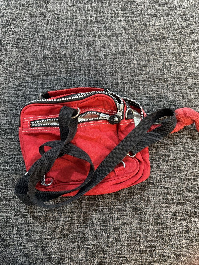 Kipling Red Crossbody Bag / Bagpack with Monkey Keychain (Category: Cross-body Bags) located in Calamba. Submitted by doublegm (Listing ID 1468517105, Image 2). Description: - Brand: Kipling - Color: Bright red with contrast white stitching - Material: Signature crinkled nylon fabric - Strap: Adjustable black crossbody strap - Storage: Multiple zipped compartments and internal slip pockets - Extras: Includes the classic fuzzy red monkey keychain 