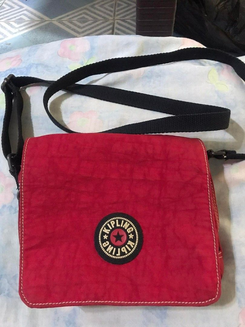 Kipling Red Crossbody Bag with Black Strap (Category: Cross-body Bags) located in Manila. Submitted by thehotness2.0 (Listing ID 1468581268, Image 1). Description: - Brand: Kipling - Color: Vibrant bright red with contrast black strap - Material: Signature durable crinkled nylon - Strap: Adjustable black shoulder/crossbody strap - Closure: Secure flap with iconic round Kipling logo patch - Capacity: Ideal daily size for phone, keys, and wallet - 