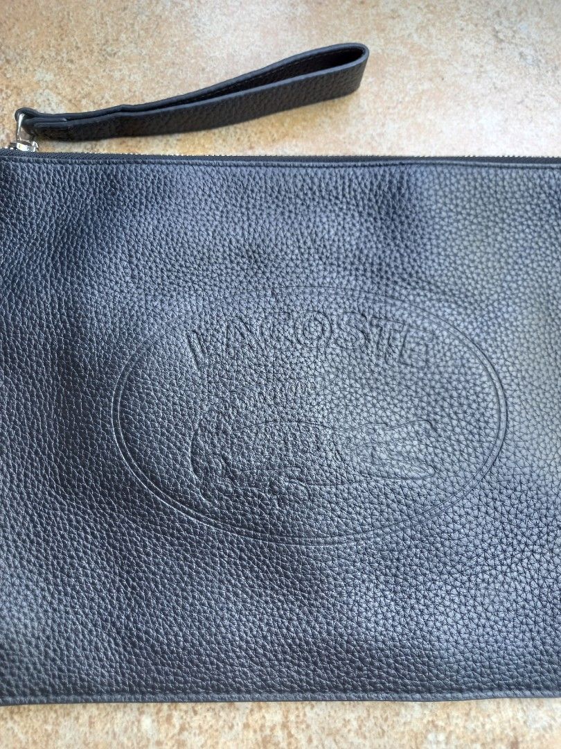 Lacoste Black Leather Pouch Clutch Bag (Category: Luxury Bags & Wallets) located in Davao. Submitted by kirk214red-50020 (Listing ID 1468531305, Image 2). Description: - Brand: Lacoste - Material: Premium black pebbled leather - Logo: Oval debossed crocodile logo on the front - Closure: Secure zip-top closure - Strap: Matching wrist strap for easy carrying - Interior: Dark fabric lining with built-in card slots - Condition: Clean stitching and st