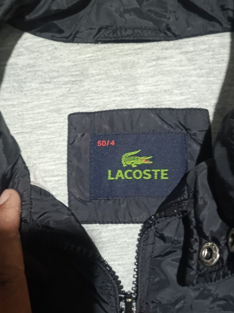 Lacoste Black Windbreaker Jacket Size 50/4 (Category: Coats, Jackets and Outerwear) located in City of Isabela. Submitted by warmbird.d06e6f (Listing ID 1468510350, Image 3). Description: - 100% Authentic Lacoste jacket in classic black - Size: 50/4 (Refer to tag) - Material: Durable nylon outer shell with soft grey polyester lining - Design: Full zip front, stand collar with snap button closure, and ribbed cuffs and hem - Pockets: Dual secure zi