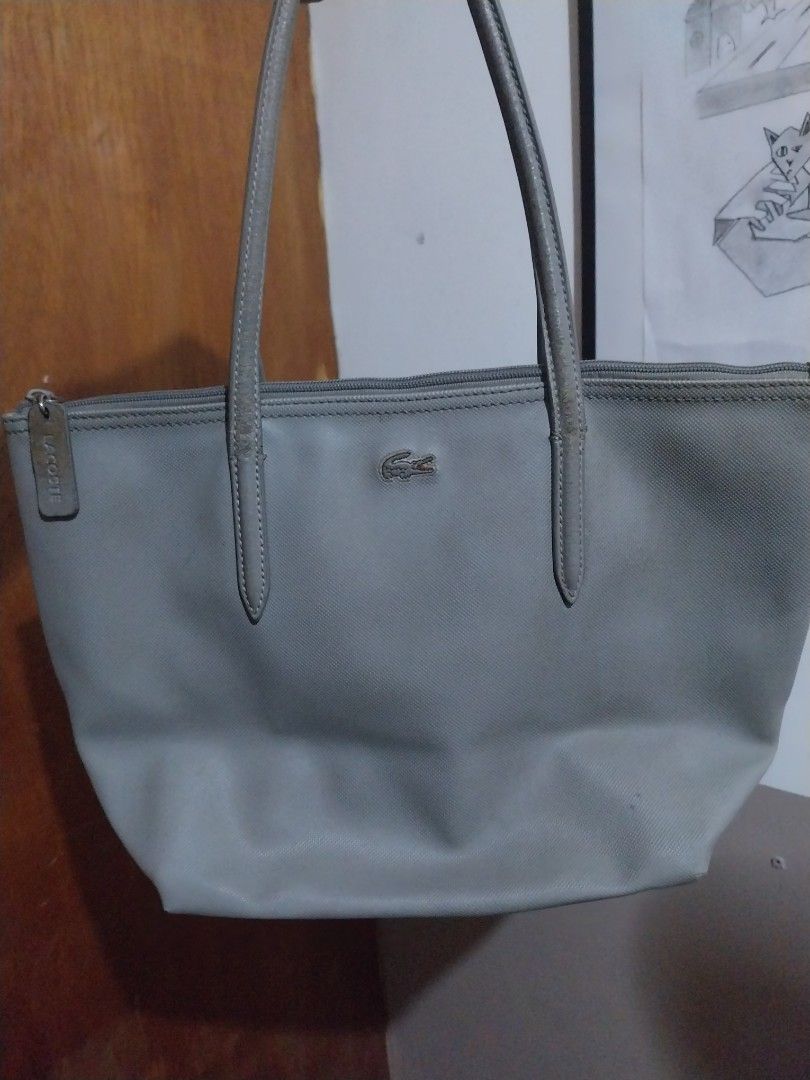 Lacoste L.12.12 Grey Tote Bag small (Category: Tote Bags) located in Manila. Submitted by j.dlh (Listing ID 1468665318, Image 1). Description: - Brand: Lacoste - Color: Classic Grey - Features: Double shoulder straps, metal crocodile logo, secure zipper closure with branded pull tab - Interior: Includes a slip pocket and branded patch - Condition/Flaws: Noticeable ink stains on the bottom exterior corner, dirt marks inside, and peeling on the str