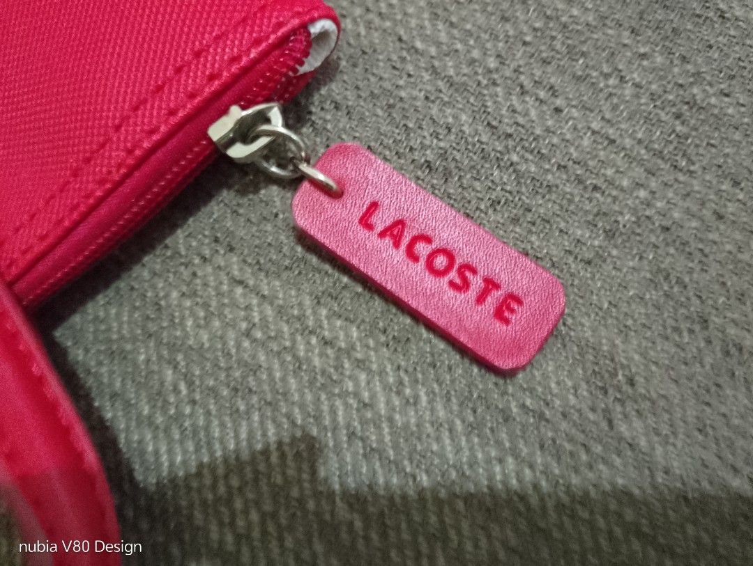 Lacoste Red Tote Bag With Crossbody Strap (Category: Tote Bags) located in Bulacan. Submitted by ann_chua84 (Listing ID 1468612674, Image 3). Description: - Authentic bright red Lacoste tote bag - Textured finish with signature metal crocodile logo on the front - Dual top handles and a convenient adjustable crossbody strap - Secure zip closure with a branded pull tab - Clean white interior fabric with repeating Lacoste text pattern.
