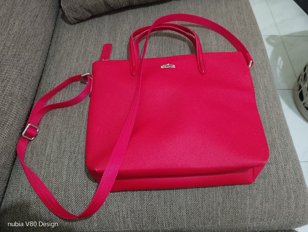 Lacoste Red Tote Bag With Crossbody Strap (Category: Tote Bags) located in Bulacan. Submitted by ann_chua84 (Listing ID 1468612674, Image 1). Description: - Authentic bright red Lacoste tote bag - Textured finish with signature metal crocodile logo on the front - Dual top handles and a convenient adjustable crossbody strap - Secure zip closure with a branded pull tab - Clean white interior fabric with repeating Lacoste text pattern.