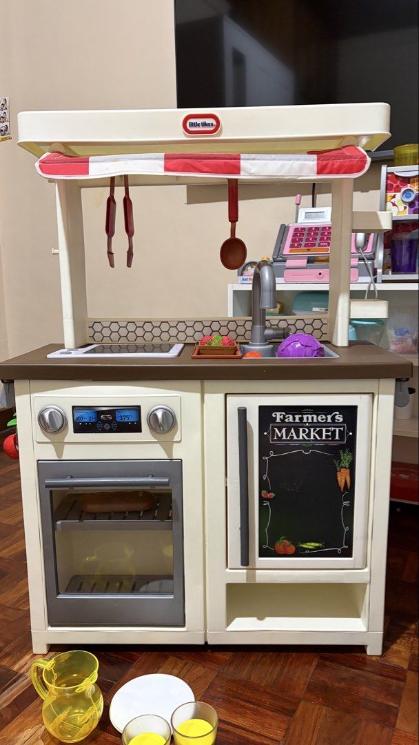 Little Tikes First Market Play Kitchen (Category: Kids Toys) located in Quezon City. Submitted by bella_ciao (Listing ID 1468638865, Image 1). Description: - Brand: Little Tikes Farmers Market play kitchen set - Features: Canopy roof, functional chalkboard cabinet door, oven with digital display graphics, stovetop, and sink faucet - Included Accessories: Hanging utensils, tray of strawberries, orange, purple cabbage, yellow pitcher, two yellow cu