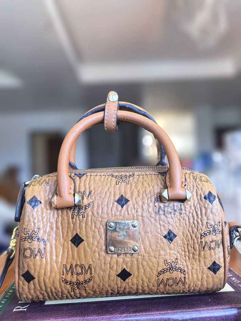 MCM Cognac Visetos Print Boston Bag (Category: Luxury Bags & Wallets) located in Cagayan de Oro. Submitted by tommygurl1218 (Listing ID 1468513332, Image 1). Description: -brown leather MCM Boston bag with classic monogram and diamond pattern - Dual top handles and secure zippered closure - Features a gold-tone front plaque engraved with serial number 62458 - Includes a detachable strap for versatile crossbody or hand-carry styling - Structured b