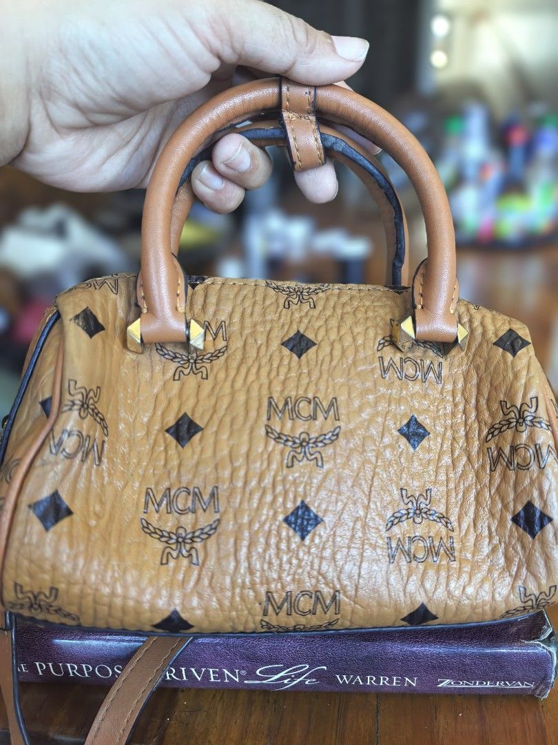 MCM Cognac Visetos Print Boston Bag (Category: Luxury Bags & Wallets) located in Cagayan de Oro. Submitted by tommygurl1218 (Listing ID 1468513332, Image 2). Description: -brown leather MCM Boston bag with classic monogram and diamond pattern - Dual top handles and secure zippered closure - Features a gold-tone front plaque engraved with serial number 62458 - Includes a detachable strap for versatile crossbody or hand-carry styling - Structured b