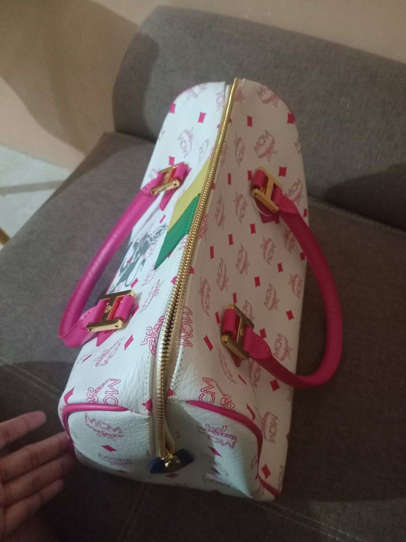 MCM White Pink Monogram Lion Graphic Duffle Handbag (Category: Luxury Bags & Wallets) located in Urdaneta. Submitted by assortedprelovedd (Listing ID 1468585701, Image 2). Description: - Material: White faux leather with pink MCM monogram print - Design: Front lion graphic with vibrant textured leather patches (yellow, green, blue, pink) - Handles & Hardware: Dual pink top handles with gold-tone hardware - Closure: Zip-around with a playful blue 