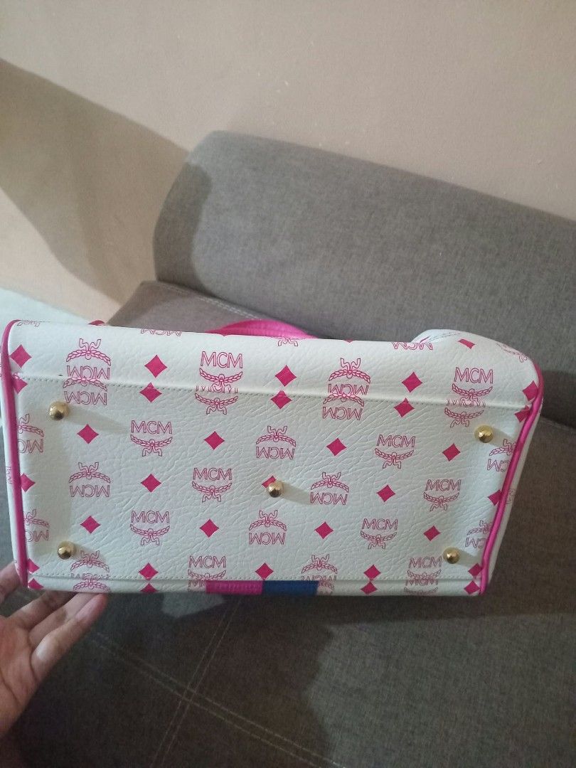MCM White Pink Monogram Lion Graphic Duffle Handbag (Category: Luxury Bags & Wallets) located in Urdaneta. Submitted by assortedprelovedd (Listing ID 1468585701, Image 3). Description: - Material: White faux leather with pink MCM monogram print - Design: Front lion graphic with vibrant textured leather patches (yellow, green, blue, pink) - Handles & Hardware: Dual pink top handles with gold-tone hardware - Closure: Zip-around with a playful blue 