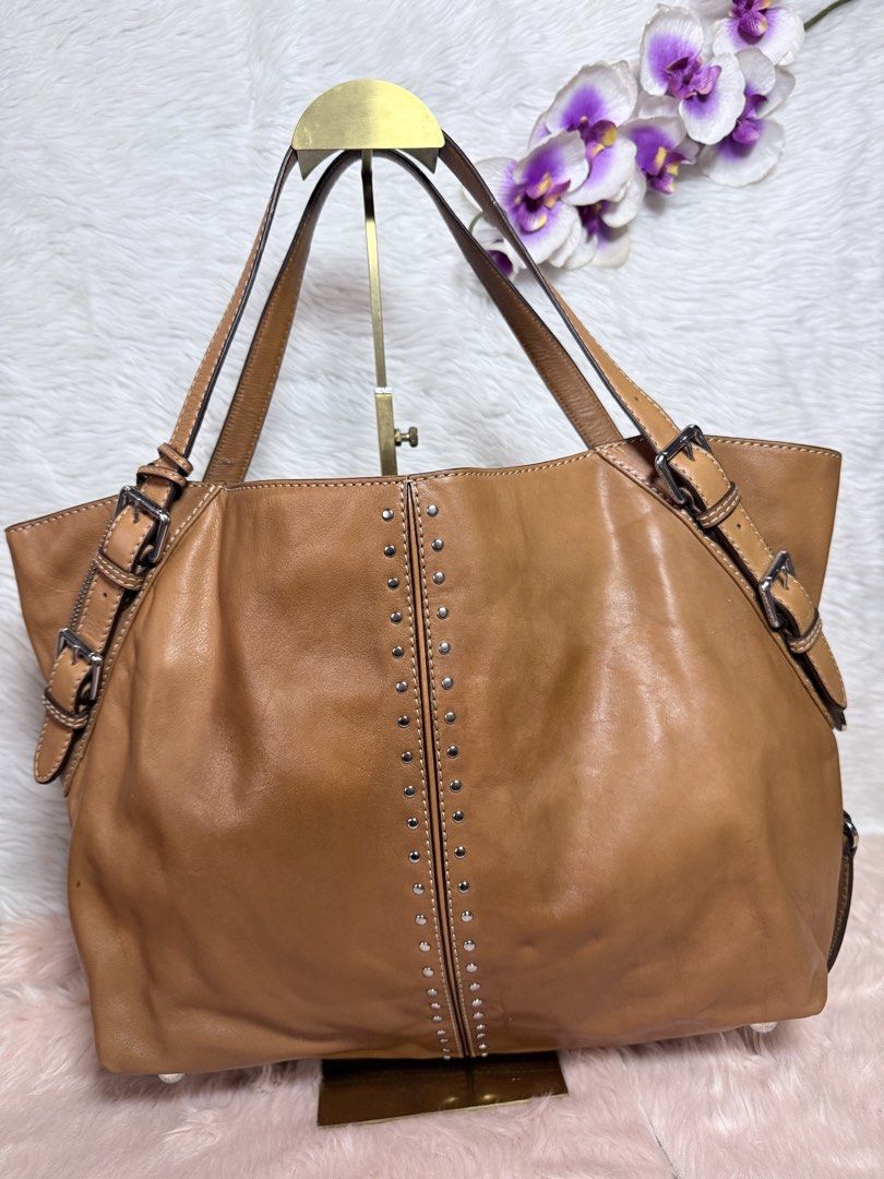 Michael Kors Astor Brown Leather Studded Shoulder Bag (Category: Luxury Bags & Wallets) located in La Trinidad. Submitted by naravincollections (Listing ID 1468582186, Image 3). Description: - Brand: Michael Kors - Material: Premium tan leather with silver-tone hardware; hardwares are still in very good condition - Design: Vertical rows of metal studs on the front, adjustable side straps, and signature MK hanging charm - Straps: Double buckled ha