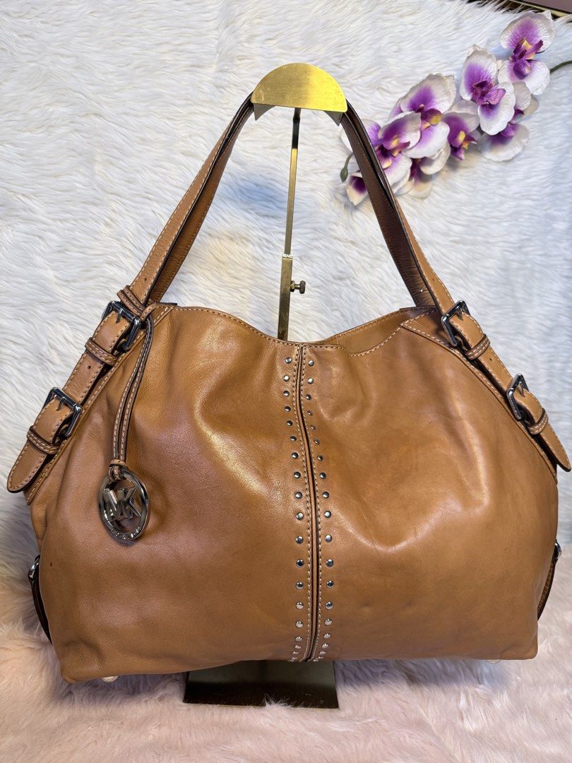 Michael Kors Astor Brown Leather Studded Shoulder Bag (Category: Luxury Bags & Wallets) located in La Trinidad. Submitted by naravincollections (Listing ID 1468582186, Image 2). Description: - Brand: Michael Kors - Material: Premium tan leather with silver-tone hardware; hardwares are still in very good condition - Design: Vertical rows of metal studs on the front, adjustable side straps, and signature MK hanging charm - Straps: Double buckled ha
