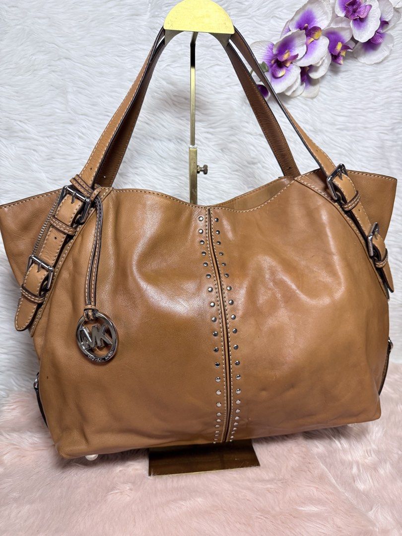 Michael Kors Astor Brown Leather Studded Shoulder Bag (Category: Luxury Bags & Wallets) located in La Trinidad. Submitted by naravincollections (Listing ID 1468582186, Image 1). Description: - Brand: Michael Kors - Material: Premium tan leather with silver-tone hardware; hardwares are still in very good condition - Design: Vertical rows of metal studs on the front, adjustable side straps, and signature MK hanging charm - Straps: Double buckled ha