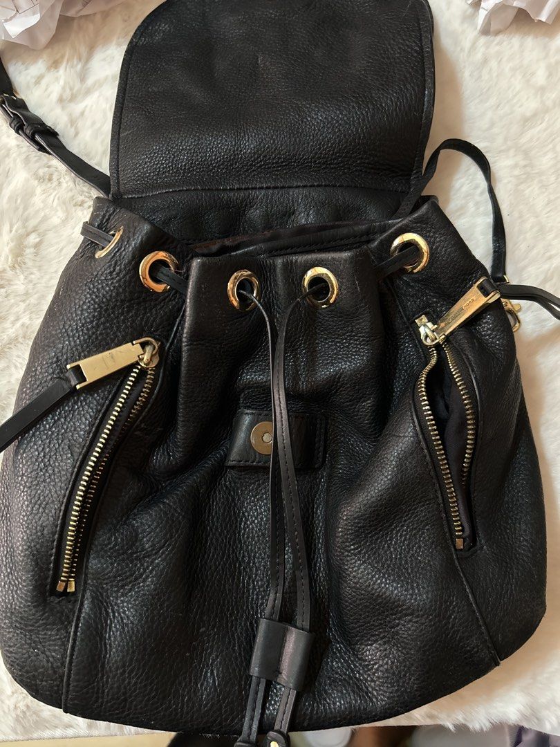 Michael Kors Black Leather Rhea Backpack (Category: Backpacks) located in Valencia. Submitted by carmzfindsph (Listing ID 1468559623, Image 1). Description: - Material: Genuine black pebble leather with gold-tone hardware - Closure: Drawstring top with a secure magnetic snap flap - Pockets: Two vertical exterior zip pockets, plus interior zip and slip compartments - Strap: Adjustable strap with lobster clasps - Interior: Fabric lined with officia