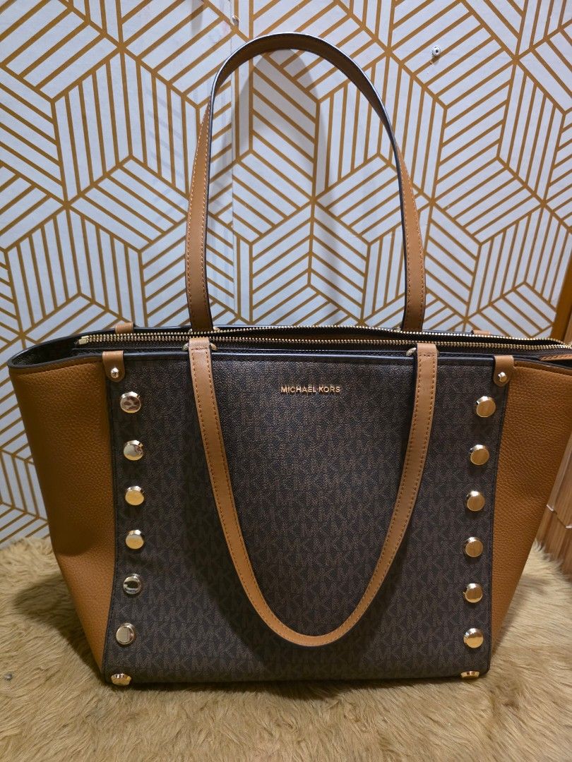 Michael Kors Brown Monogram Tote Bag with Studs (Category: Luxury Bags & Wallets) located in Santo Tomas. Submitted by FashionshopByA (Listing ID 1468515579, Image 1). Description: - Authentic brown Michael Kors tote bag - Signature monogram print with chic pebble leather panels - Elegant gold-tone hardware and decorative front metal studs - Comfortable dual shoulder straps - Secure zippered top closure - Spacious interior easily fits daily essen